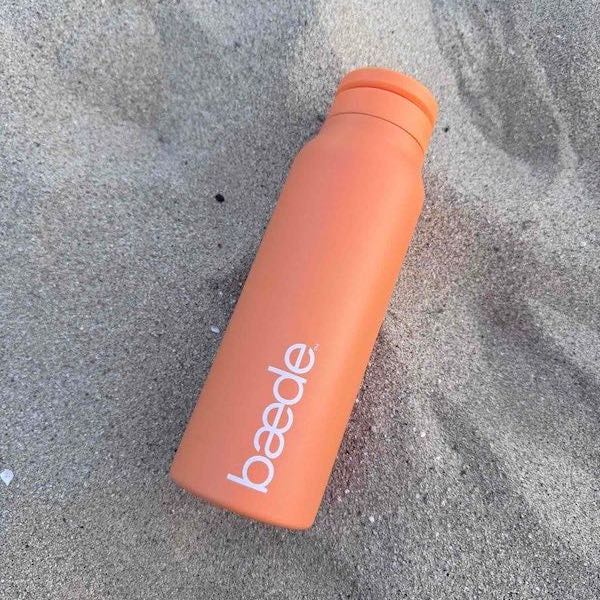 Orange metal water bottle withthe brand baede in white 